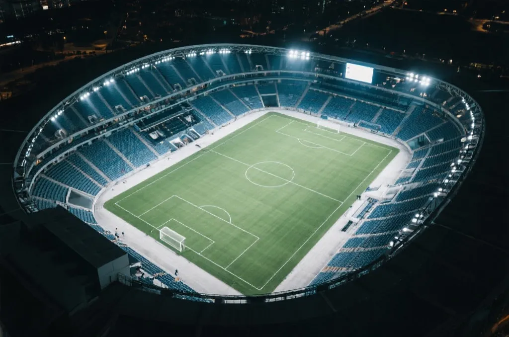 An aerial view of an empty modern sports arena under bright stadium lights, cinematic and professional photography style